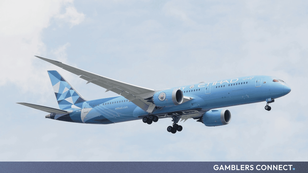 An Etihad Airways passenger airplane flying against a cloudy sky, representing global sports sponsorship and aviation.
