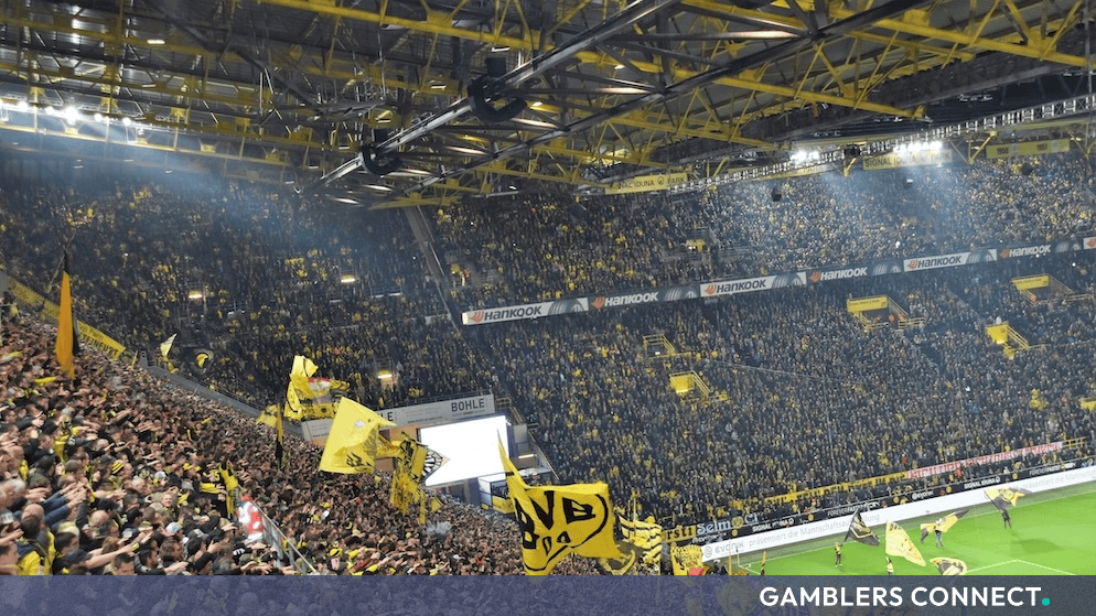 Packed stadium stands filled with Borussia Dortmund supporters waving yellow flags representing sports integrity and commercial partnership due diligence